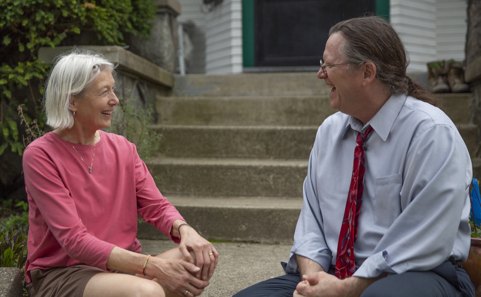 Dave Bulkowski sitting on a front-porch step, laughing with a Grand Rapids neighbor.